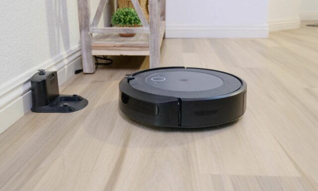 Aspirateur robot noir sur un parquet clair à côté de sa base de charge