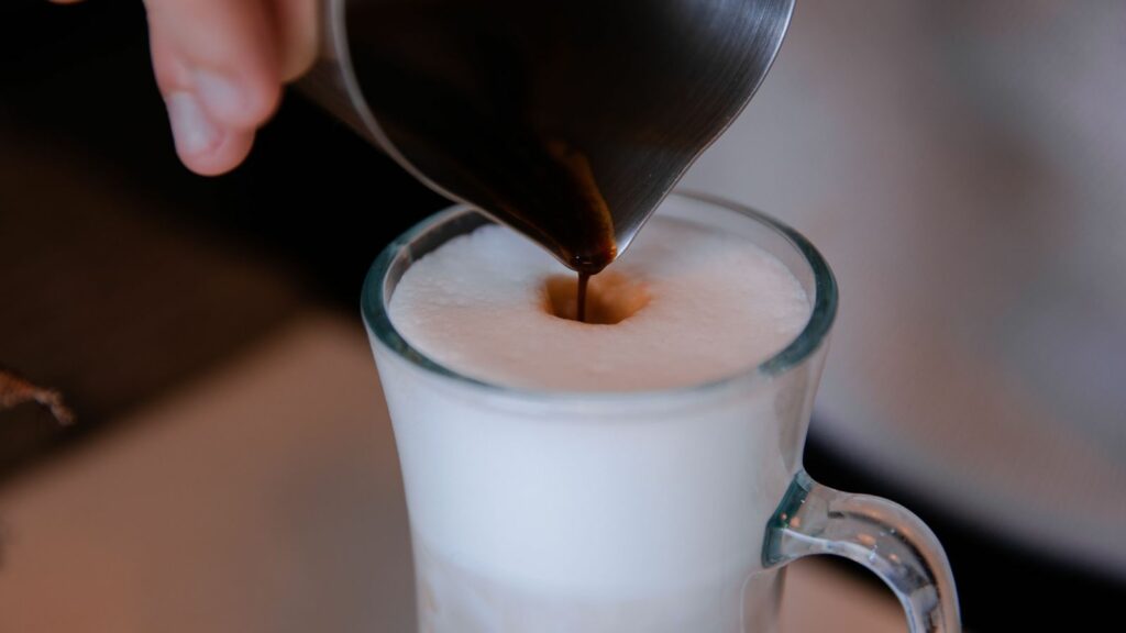 Café versé dans un verre de lait mousseux pour préparer un cappuccino