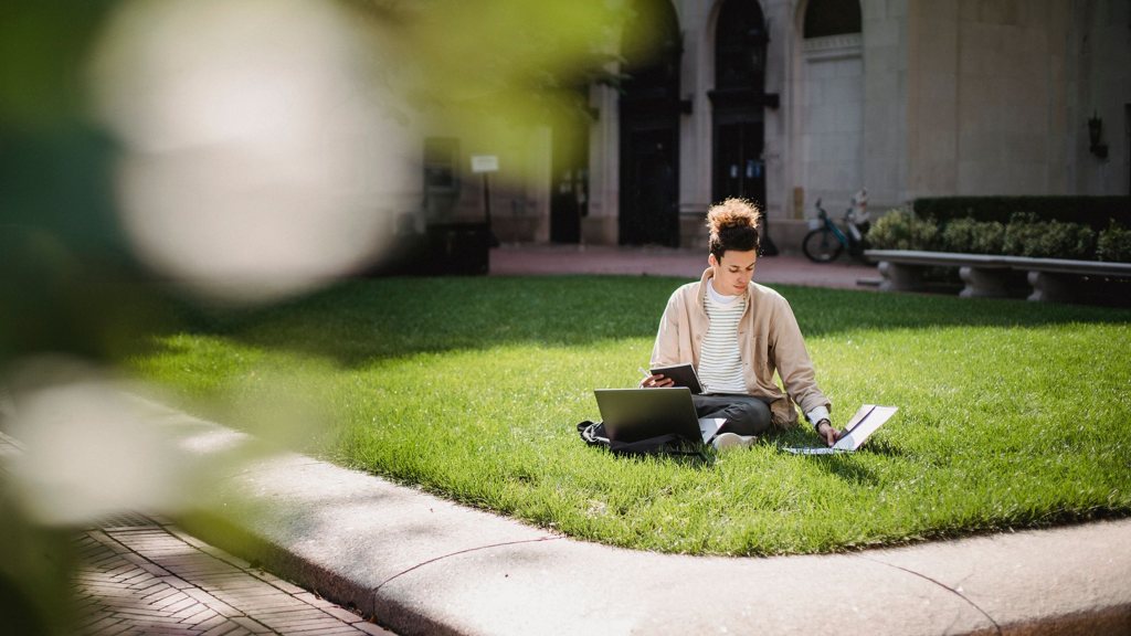 Étudiant assis sur une pelouse de campus avec son ordinateur portable