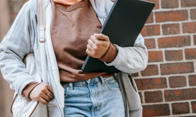 Étudiante tenant un ordinateur portable sous le bras devant un mur de briques