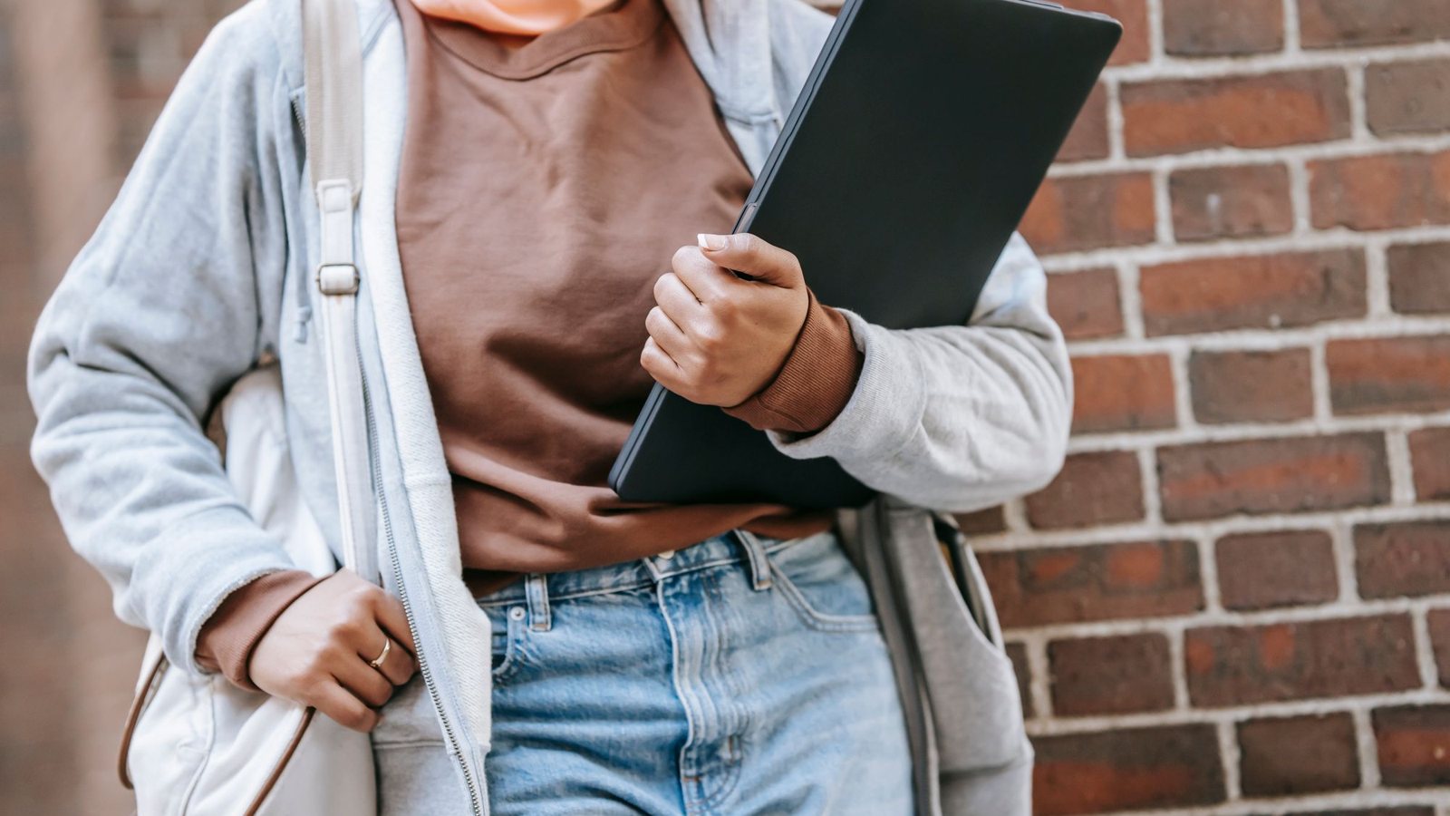 Étudiante tenant un ordinateur portable sous le bras devant un mur de briques