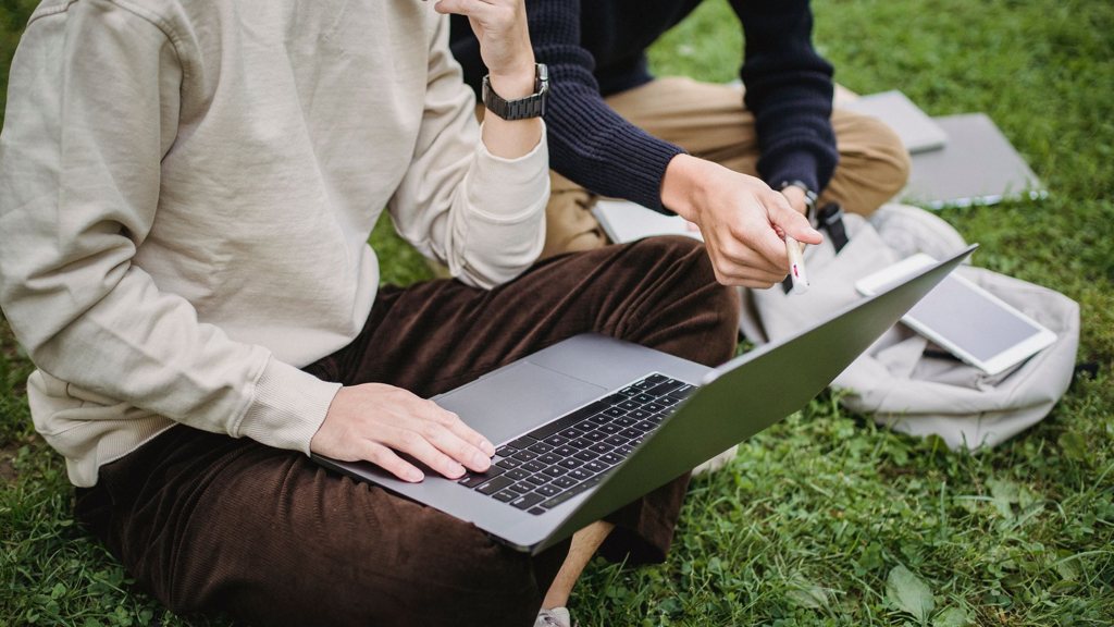 Étudiants travaillant ensemble sur un ordinateur portable assis dans l'herbe