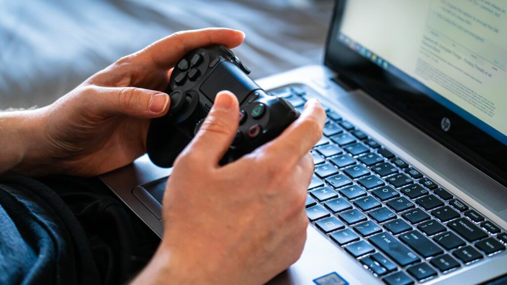 Mains tenant une manette de jeu devant un ordinateur portable